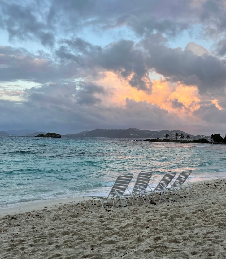 four empty chairs sitting on a beach at dusk with a colorful sky